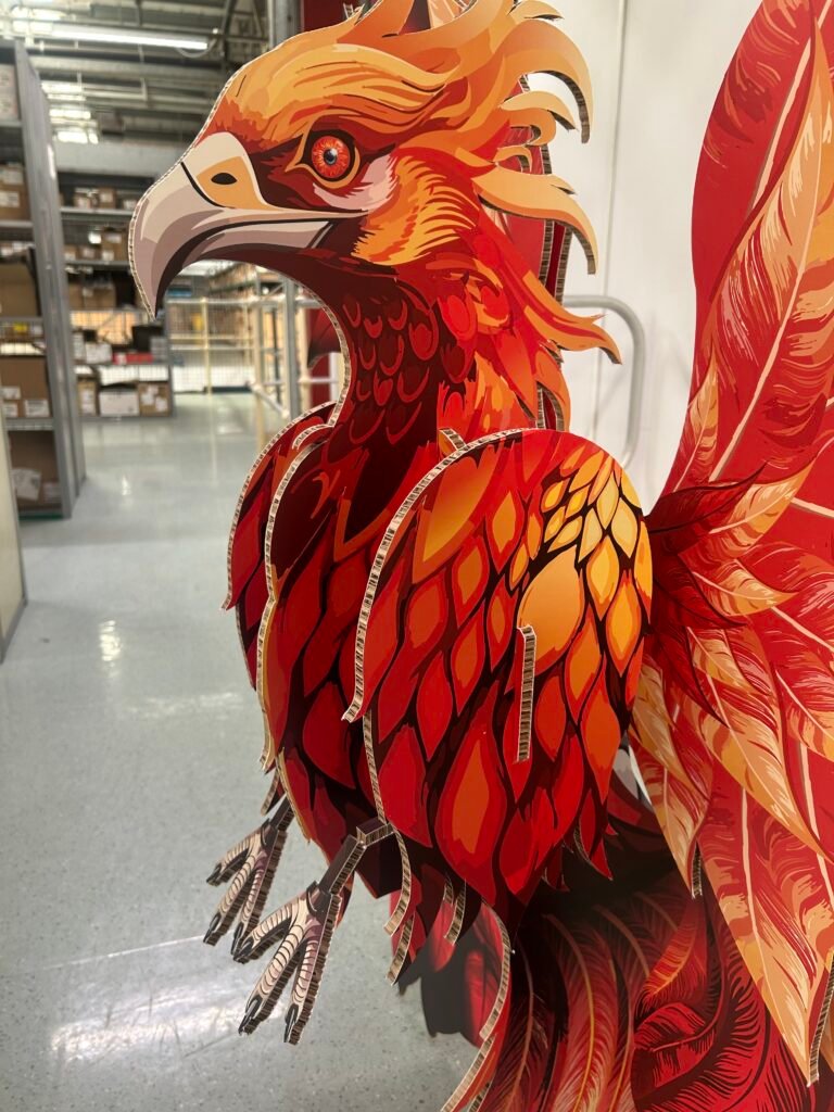 Close-up of a bright red‑orange stylized phoenix cutout on display in a store, showing detailed feathers and a sharp beak.